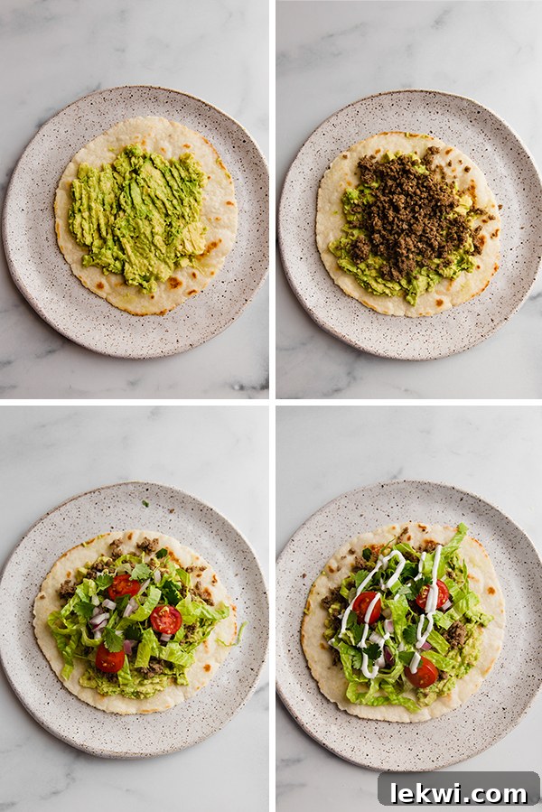 Close-up of a hand assembling a grain-free tostada, layering mashed avocado, ground beef, and colorful vegetables.