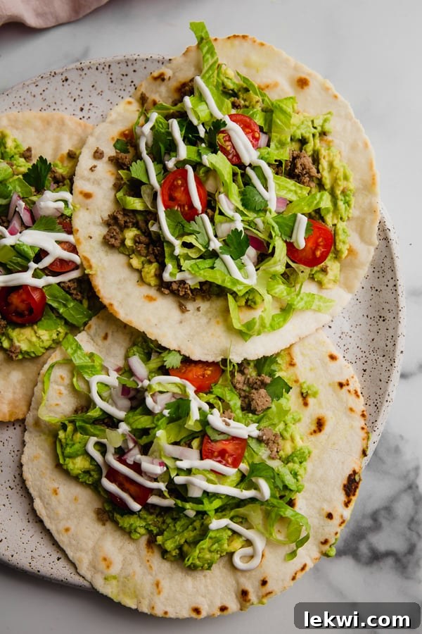 A plate featuring two Paleo Ground Beef Tostadas, garnished with fresh cilantro and a lime wedge.