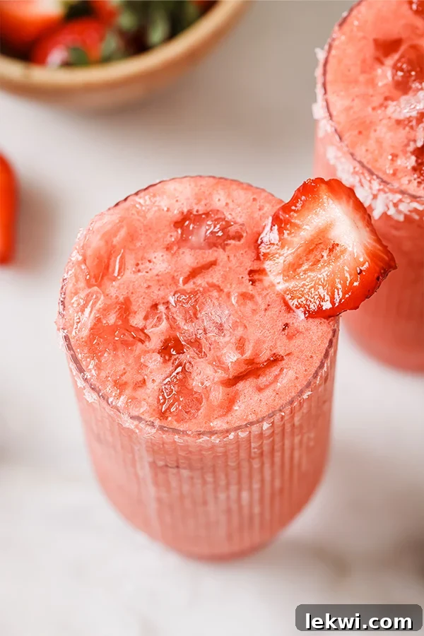 Glass of strawberry margarita mocktail with ice, garnished with a fresh strawberry and lime wedge.