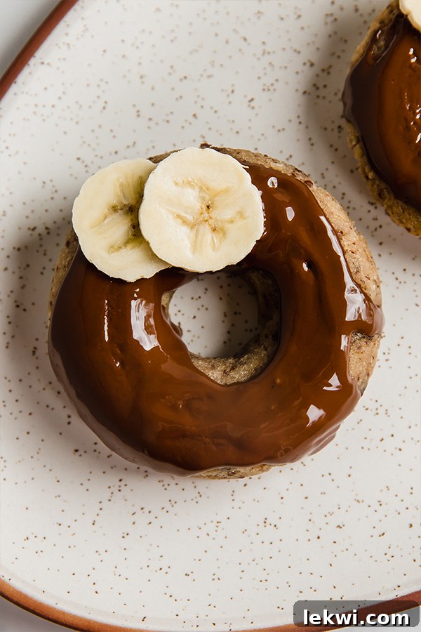 Three beautifully glazed banana bread donuts, garnished with fresh banana slices, arranged on a rustic plate.