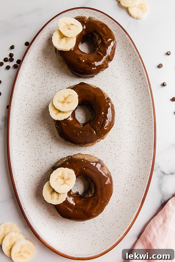 A trio of banana bread donuts displayed invitingly on a simple plate, highlighting their appealing texture and shape.