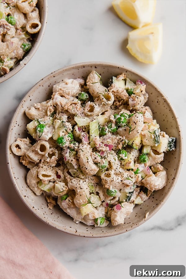 Bowl of tuna pasta salad on a marbled surface, with a fork ready to serve.