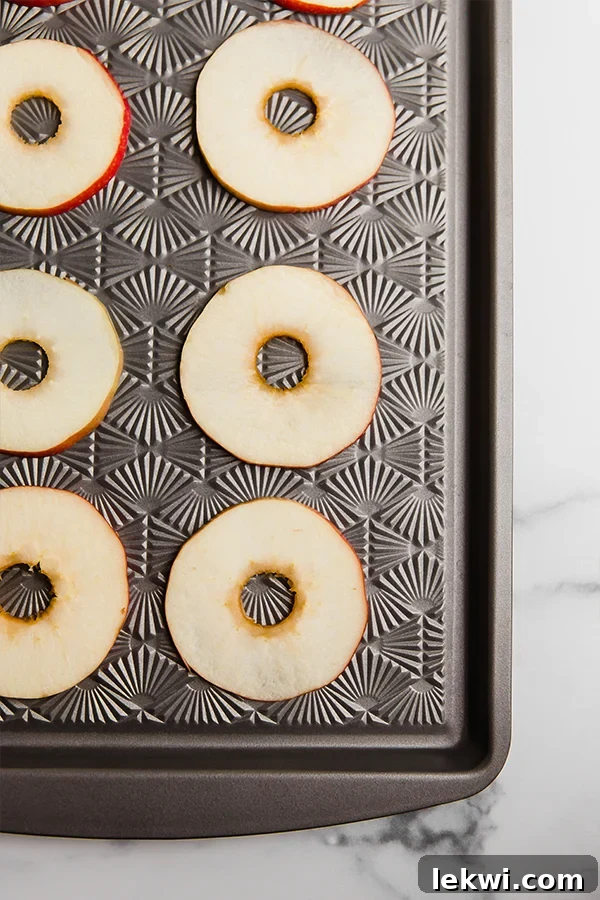Neatly sliced apple rings, with the cores removed, arranged on a sheet pan, perfectly prepped for adding toppings.