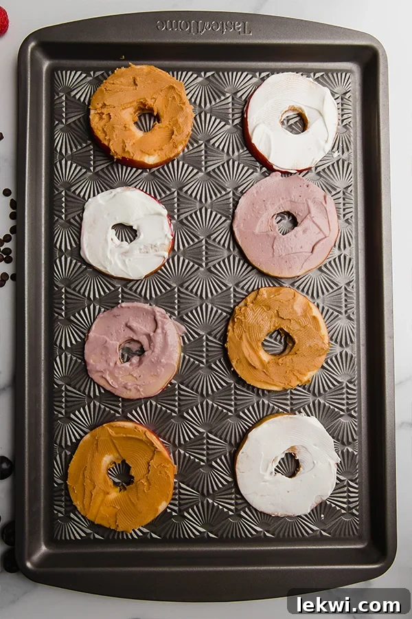 Freshly sliced apple rings generously spread with creamy almond butter and rich coconut yogurt, ready for delightful toppings.