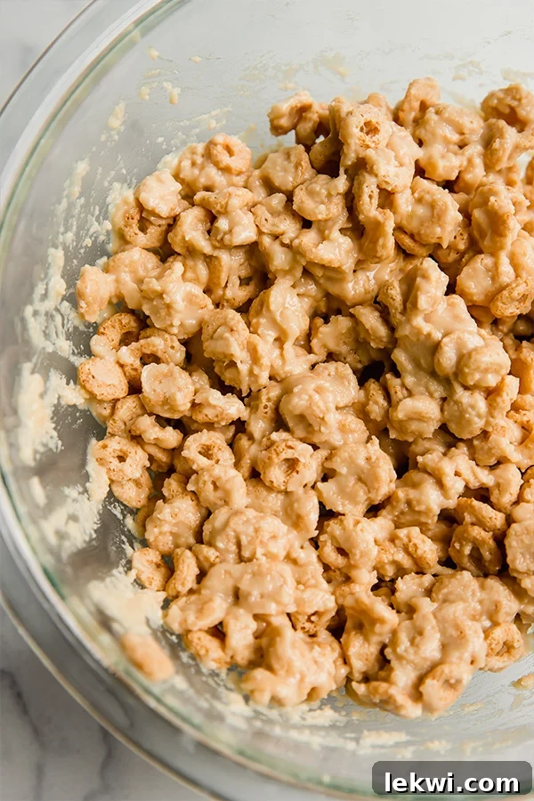 Cereal mixed with coconut butter, honey, and other ingredients in a large bowl, ready to be combined.