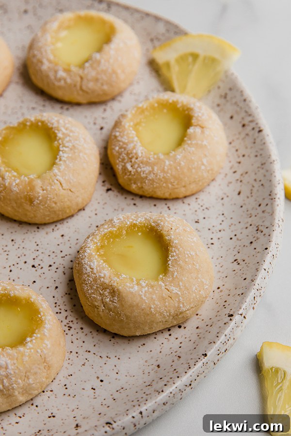 Close-up of lemon bar thumbprint cookies on a plate, with a sprinkle of corn-free powdered sugar on top.