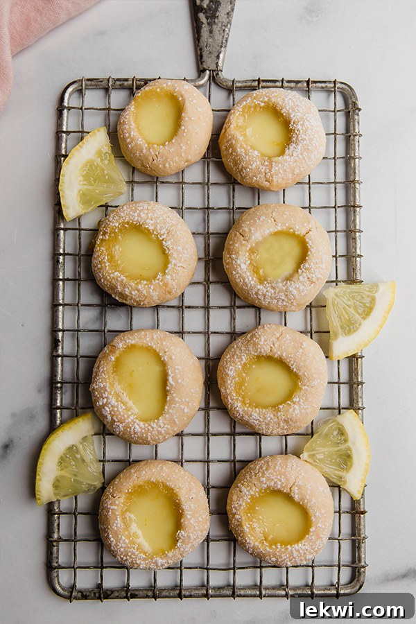 Lemon bar thumbprint cookies arranged artfully on a wire rack, with some powdered sugar on top.