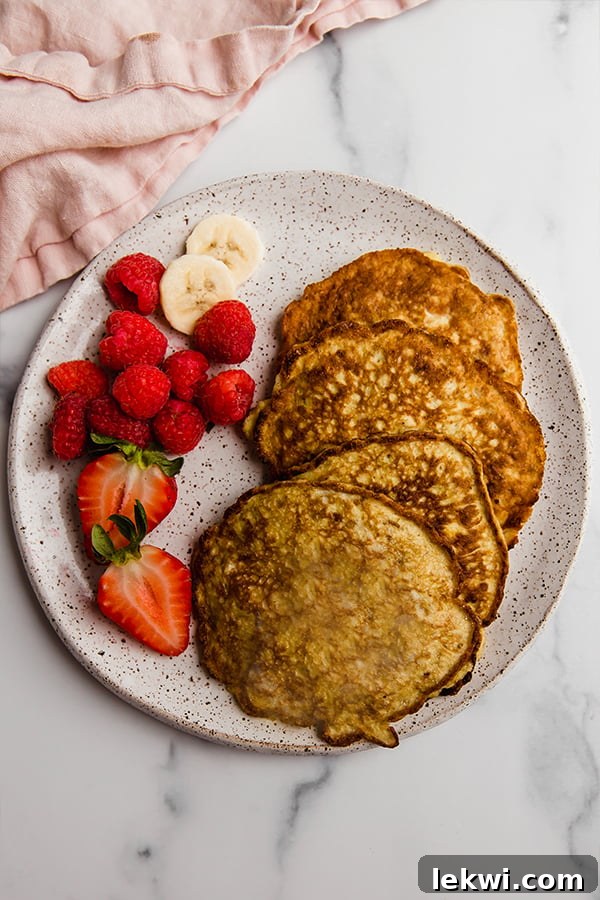 A stack of golden brown 3-ingredient banana pancakes topped with fresh berries and sliced bananas on a white plate, ready for breakfast.