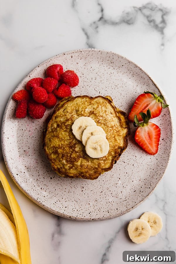 A plate of freshly cooked 3-ingredient banana pancakes topped with a sliced banana, ready to be served for breakfast.