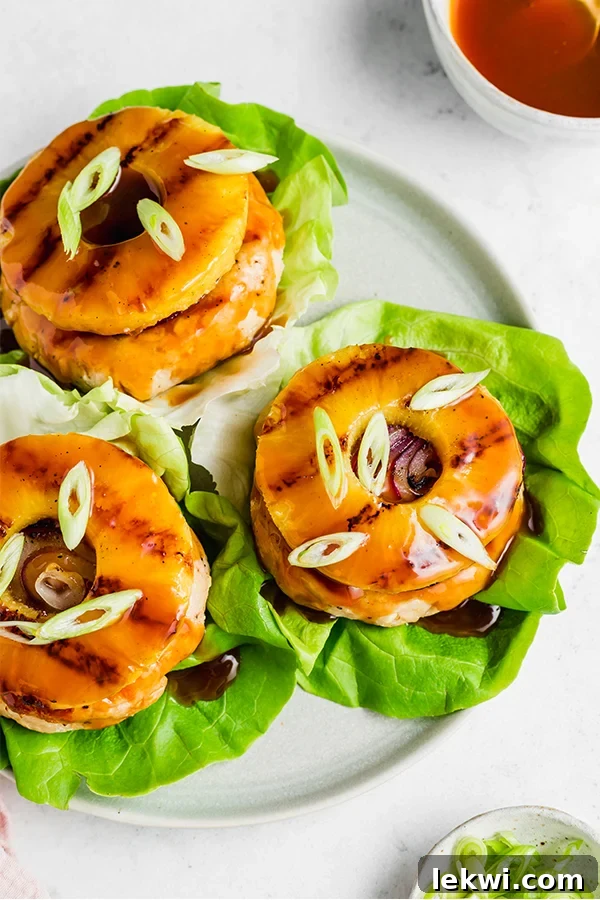 Sweet and sour chicken burgers served on fresh lettuce wraps, garnished with vibrant green onions and grilled pineapple slices, embodying a healthy and flavorful summer meal.