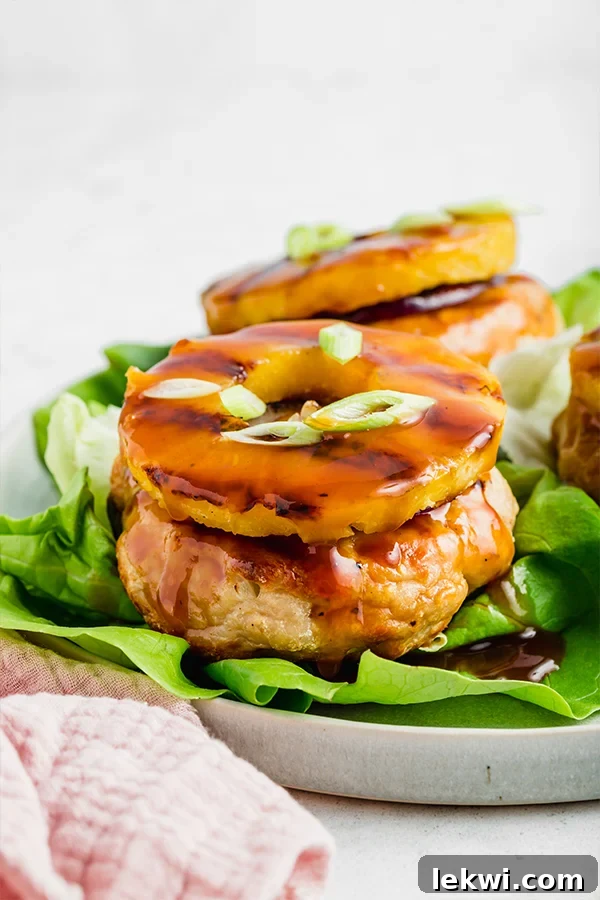 An inviting close-up of a perfectly grilled sweet and sour chicken burger, topped with a glistening pineapple ring and nestled on a vibrant lettuce leaf, ready to be enjoyed.