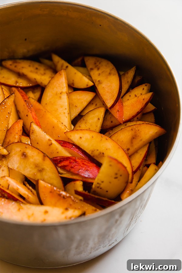 Close-up of sliced peaches simmering gently with coconut sugar in a metal saucepan, creating a sweet and tender filling for cobbler.