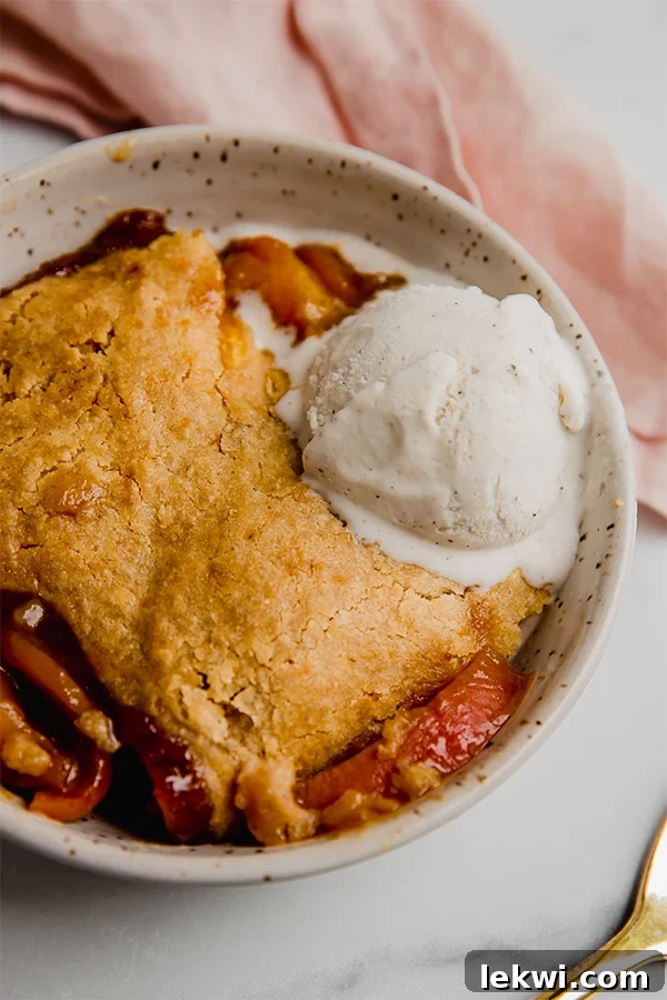 A bowl of freshly baked Paleo & AIP Peach Cobbler topped with a scoop of dairy-free vanilla ice cream, ready to be enjoyed.