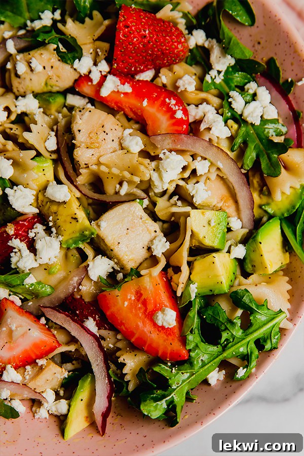 Close-up view of the Strawberry Balsamic Pasta Salad in a pink bowl, highlighting the fresh strawberries and chicken.