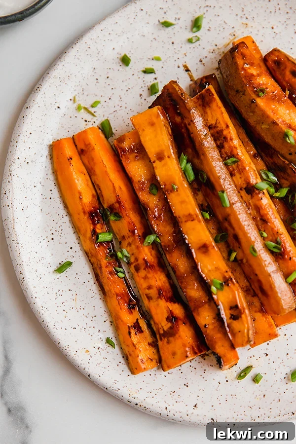 Grilled sweet potato fries served on a white plate with a side of dipping sauce and fresh chives, ready to be enjoyed at a summer cookout.