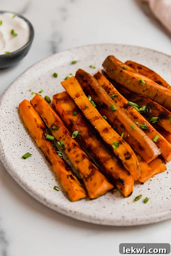 Close-up of perfectly grilled sweet potato fries, golden brown and slightly charred, on a plate with a blurry background, emphasizing their delicious texture.