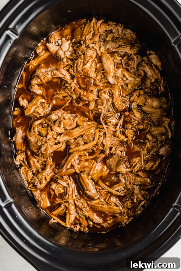 Pulled pork in the insert of a slow cooker, shredded and ready to serve.
