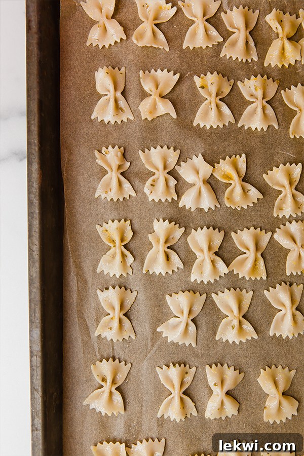 Seasoned pasta arranged in a single layer on a parchment-lined baking sheet, ready for baking.