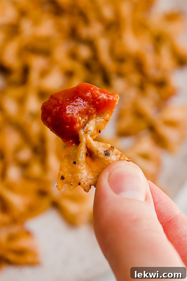 A hand holding a perfectly crispy pasta chip dipped in rich marinara sauce, showcasing its crunchy texture.