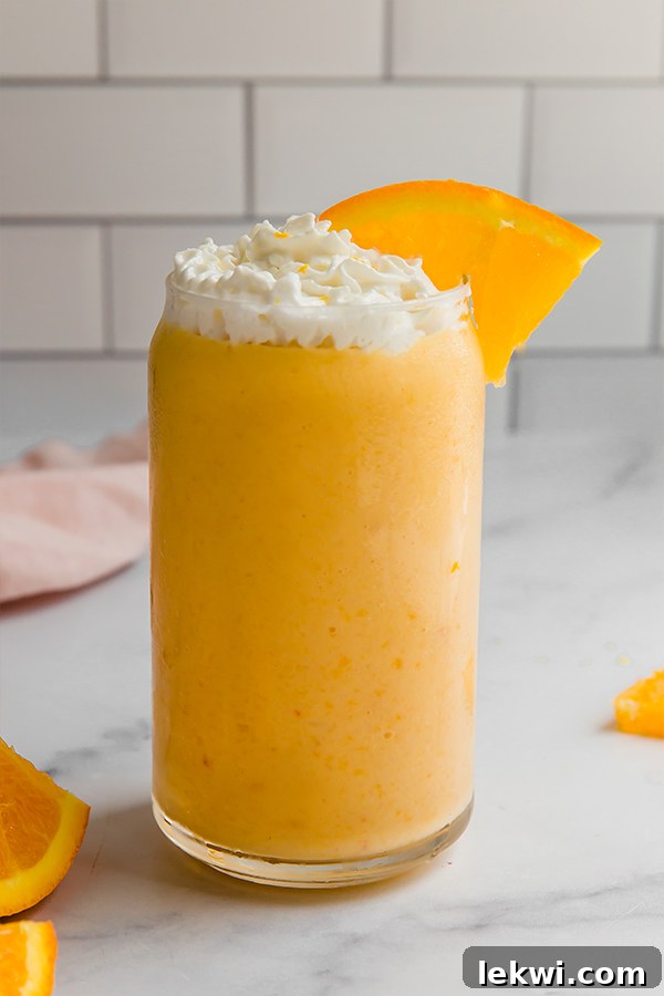 A healthy orange creamsicle smoothie in a tall glass, garnished with creamy whipped topping and a slice of fresh orange, ready to be enjoyed.