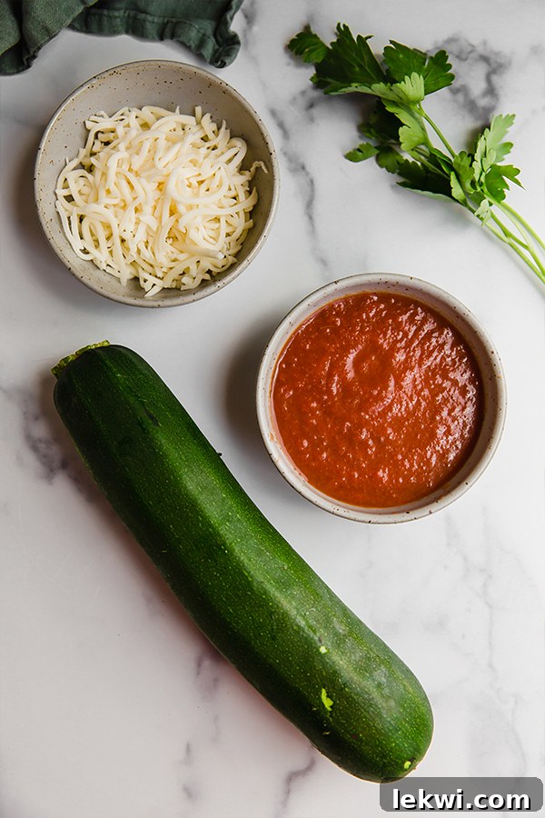 Fresh ingredients for mini zucchini pizza bites laid out on a kitchen counter, including sliced zucchini, marinara sauce, cheese, and Italian chomps stick.