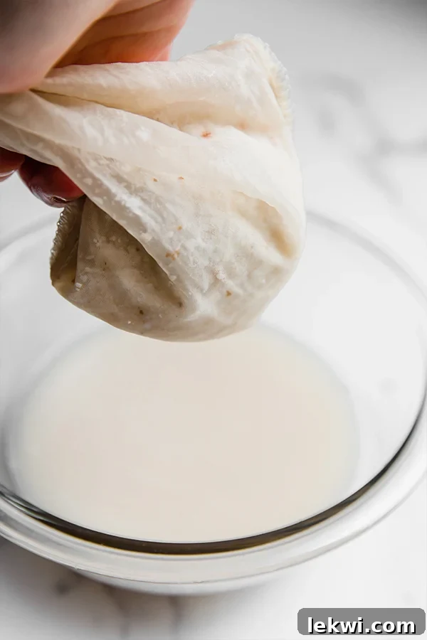 The process of straining freshly blended coconut milk through a nut milk bag into a glass bowl.