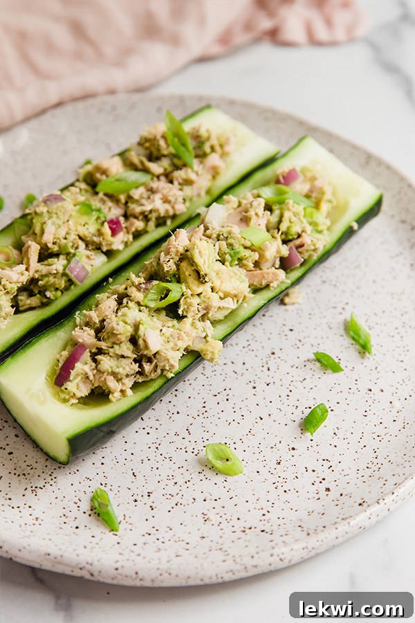 Two perfectly arranged avocado tuna salad cucumber boats on a plate, garnished and ready.