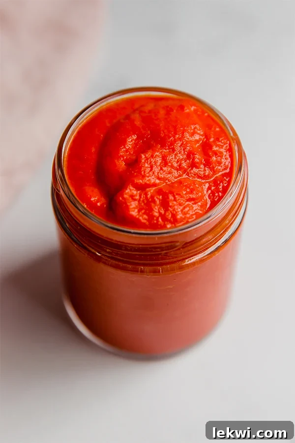 Close-up of tomato-free AIP ketchup in a glass jar, highlighting its rich color and smooth texture.