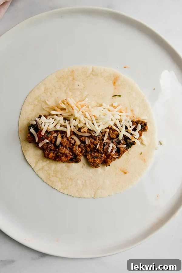 Tortilla on a plate with filling and cheese, ready to be rolled.