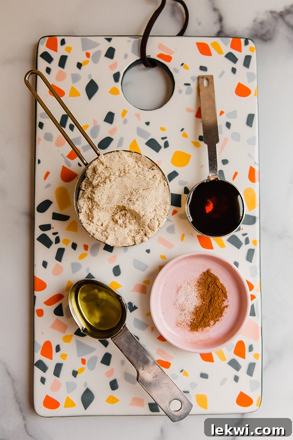 Individual ingredients for homemade tigernut butter, including tigernut flour, avocado oil, maple syrup, cinnamon, and sea salt, neatly arranged on a colorful cutting board.