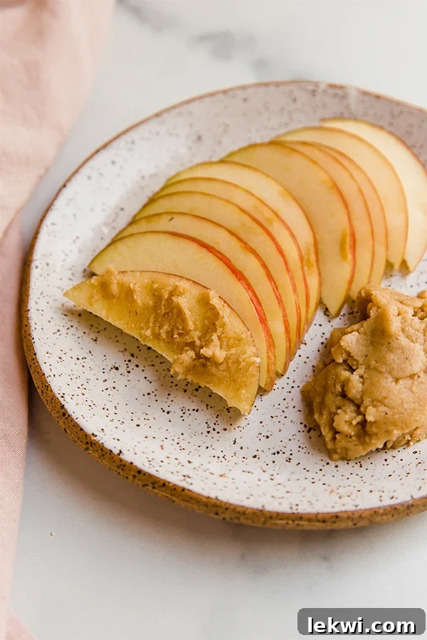 Fresh apple slices arranged on a plate with a generous dollop of homemade tigernut butter, highlighting a simple and healthy snack idea.