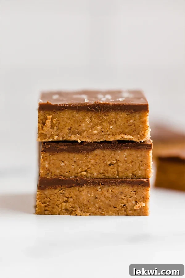 A stack of three homemade almond butter bars, layered with chocolate, rests on a kitchen counter, ready to be enjoyed.
