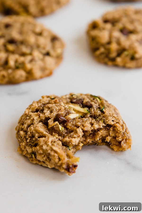 A single, perfectly baked oatmeal zucchini cookie with a bite taken out, revealing its soft interior, rich chocolate chips, and tempting chewiness on a rustic counter.