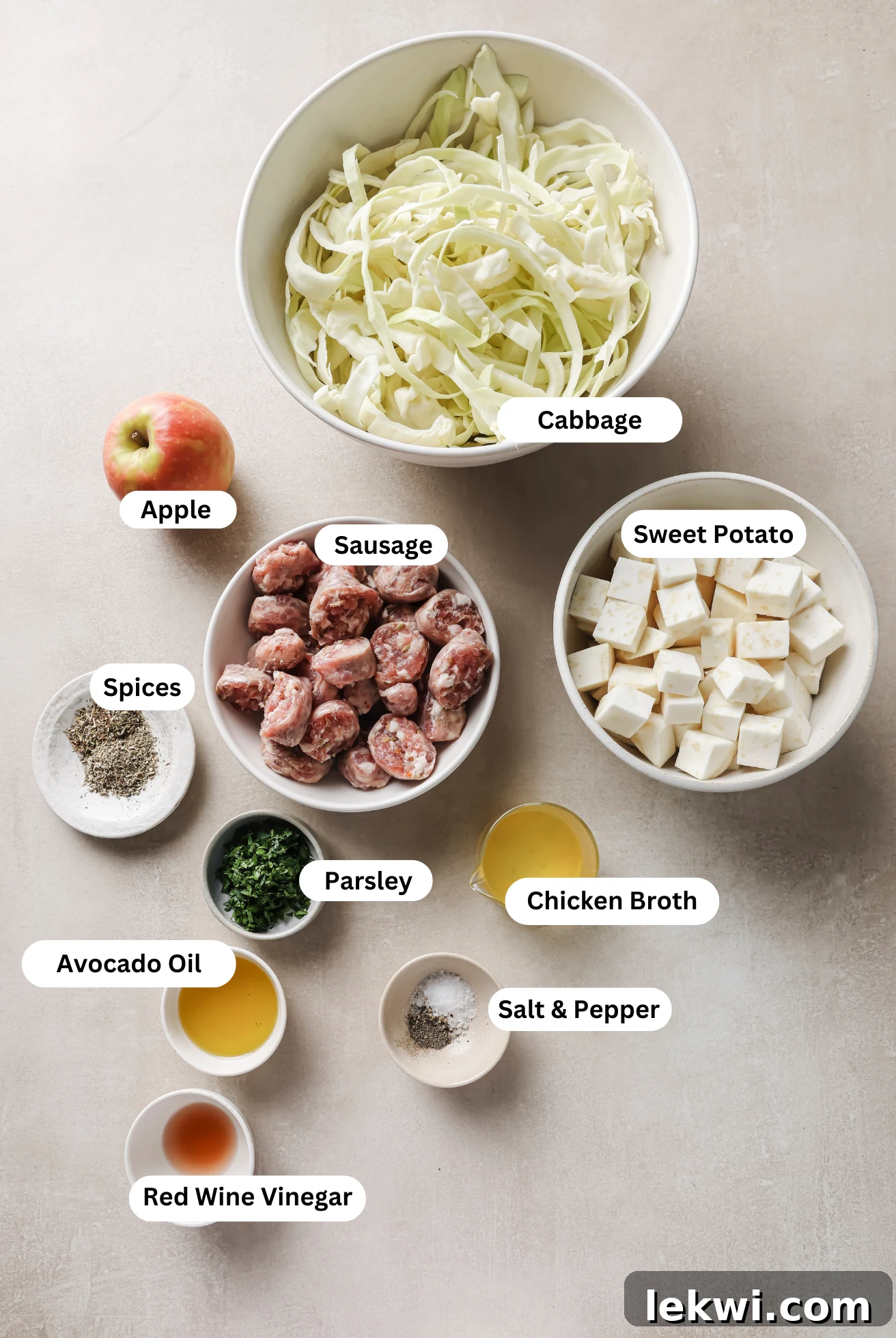 Fresh ingredients laid out on a wooden surface, including cubed sweet potato, sliced sausage, a whole apple, shredded cabbage, and fresh parsley, all ready for the Cabbage and Sausage Breakfast Skillet.