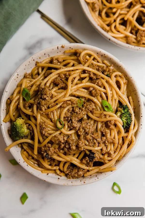 Top-down view of Mongolian ground beef with noodles served in a beautiful ceramic bowl, adorned with green onions and chopsticks.