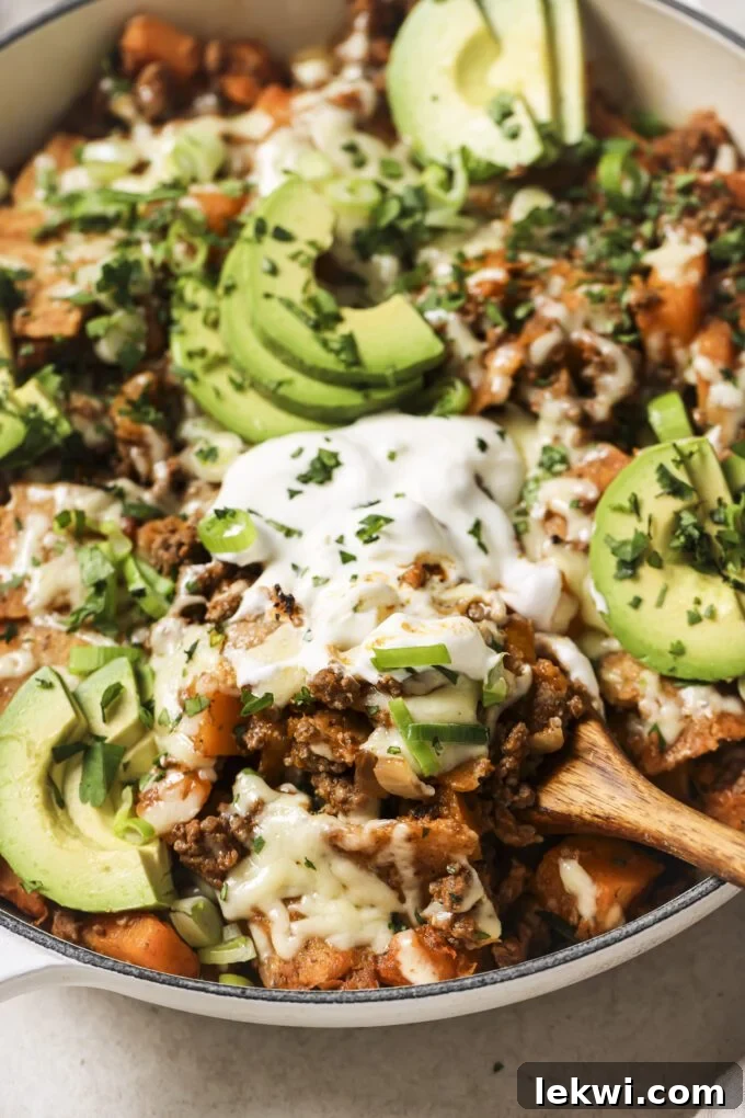 Enchilada skillet topped with avocado and chopped parsley, with a wooden spoon.