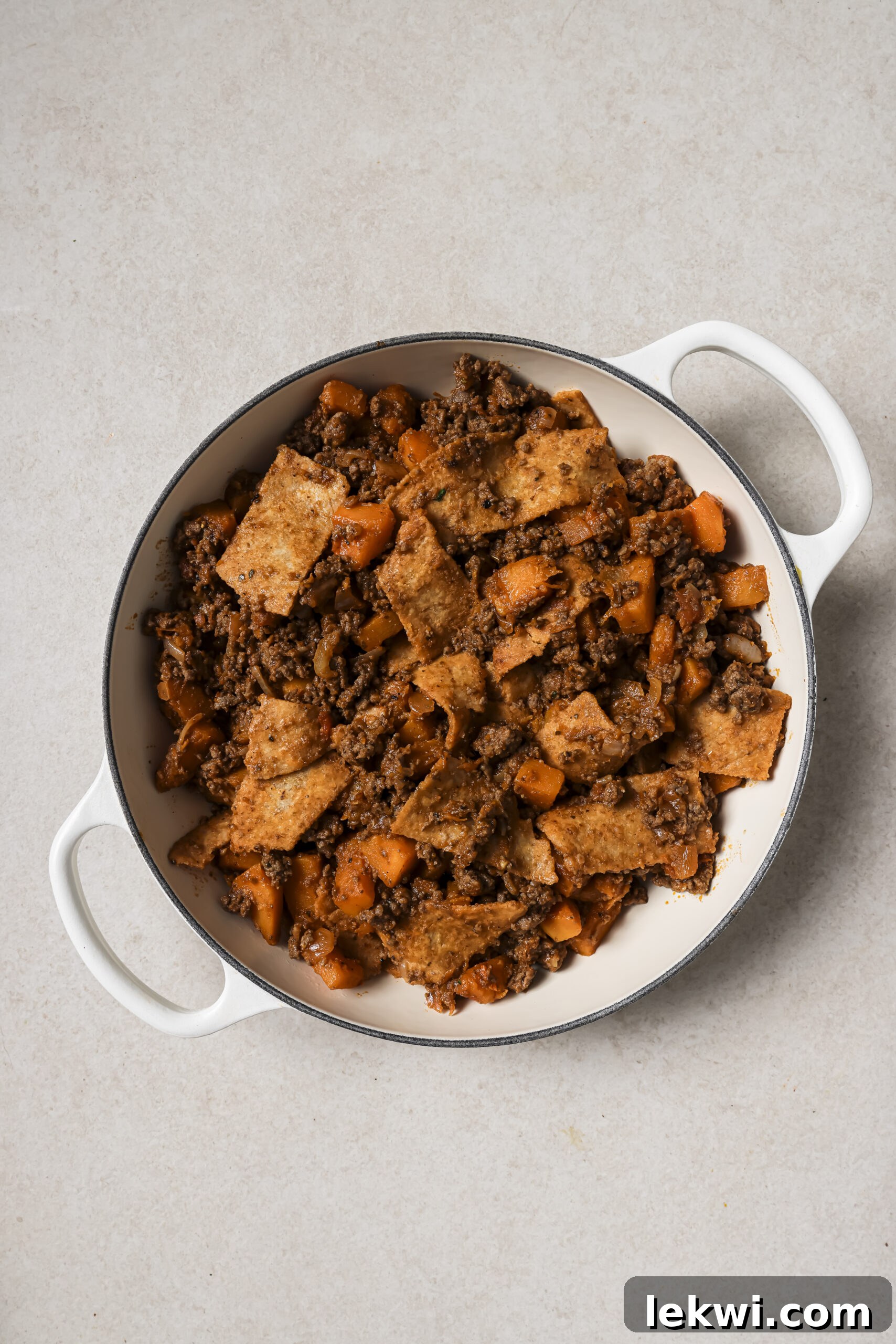 A large white pan with cooked ground beef, sweet potato and sliced tortillas.