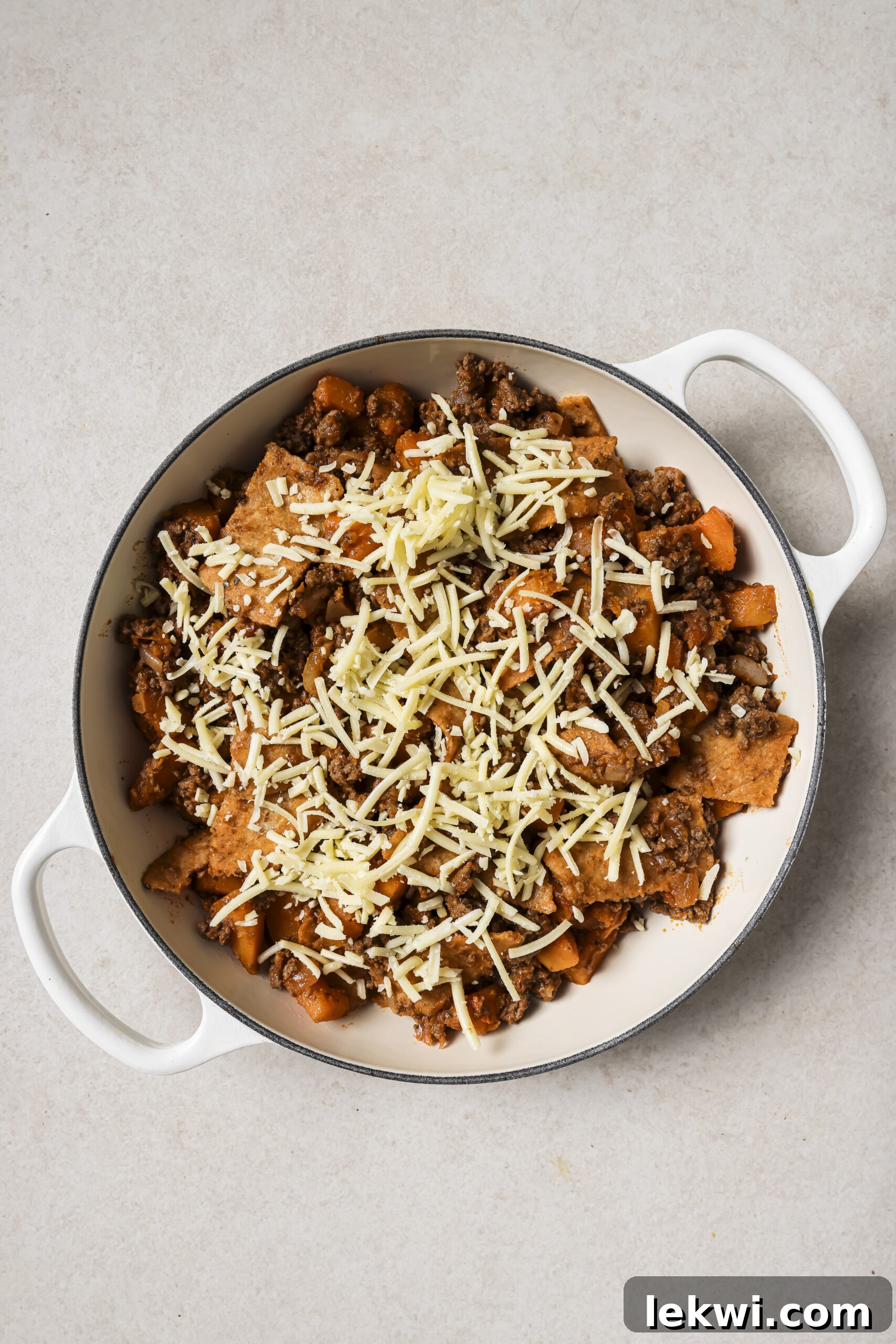 A large white pan with cooked ground beef, sweet potato, sliced tortillas and shredded cheese.
