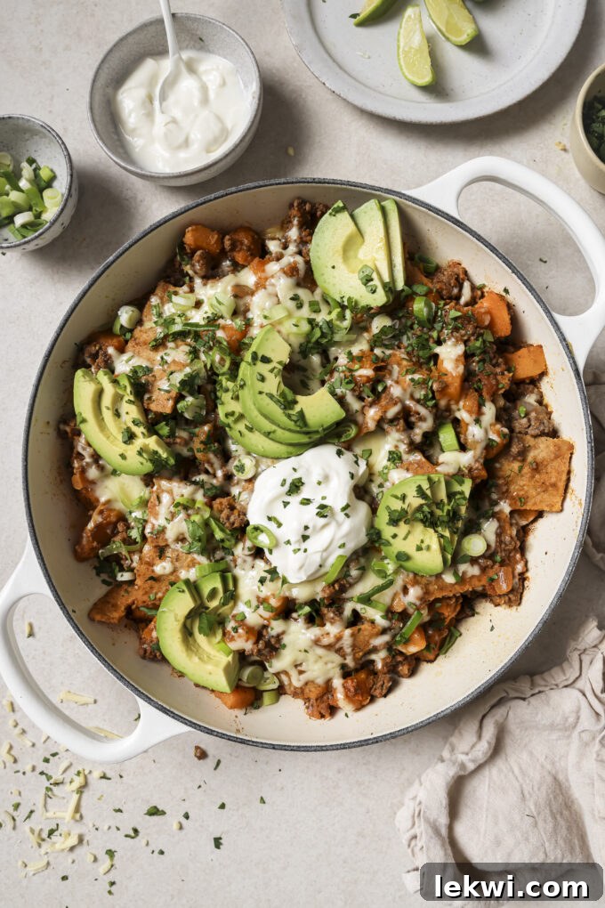 Enchilada skillet topped with avocado and chopped cilantro in a white pot.