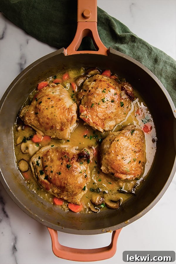 A close-up, top-down view of perfectly cooked chicken thighs in a simmering, creamy fricassee sauce, surrounded by colorful vegetables, ready to be served.