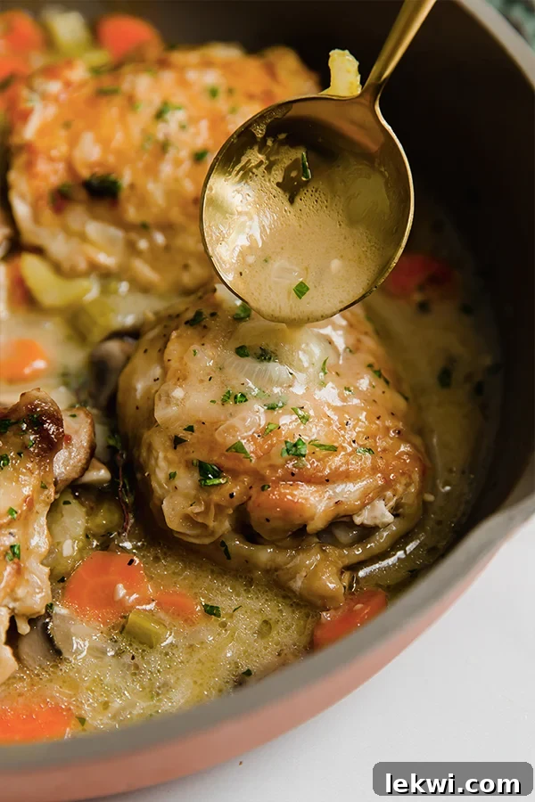 A close-up shot of a spoon gently basting a succulent piece of chicken with the rich, creamy fricassee sauce directly in the pan.