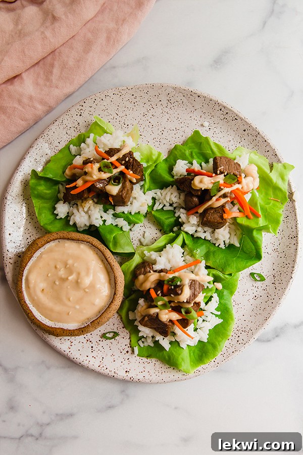 A beautifully arranged plate showcasing assembled hibachi steak lettuce wraps, accompanied by a small cup of the creamy mustard sauce for dipping.