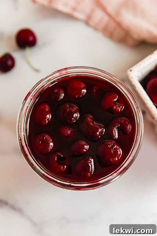 Top view of homemade maraschino cherries in a clear glass jar, glistening in their natural syrup, ready for storage or serving.