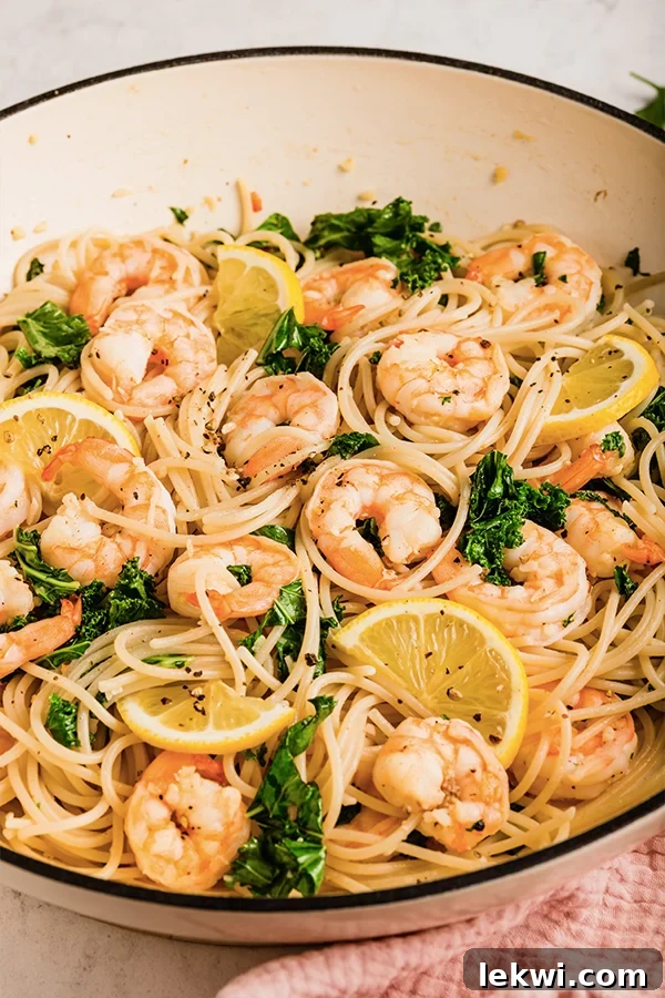 Lemon garlic shrimp pasta finished cooking in a large pan with lemon slices