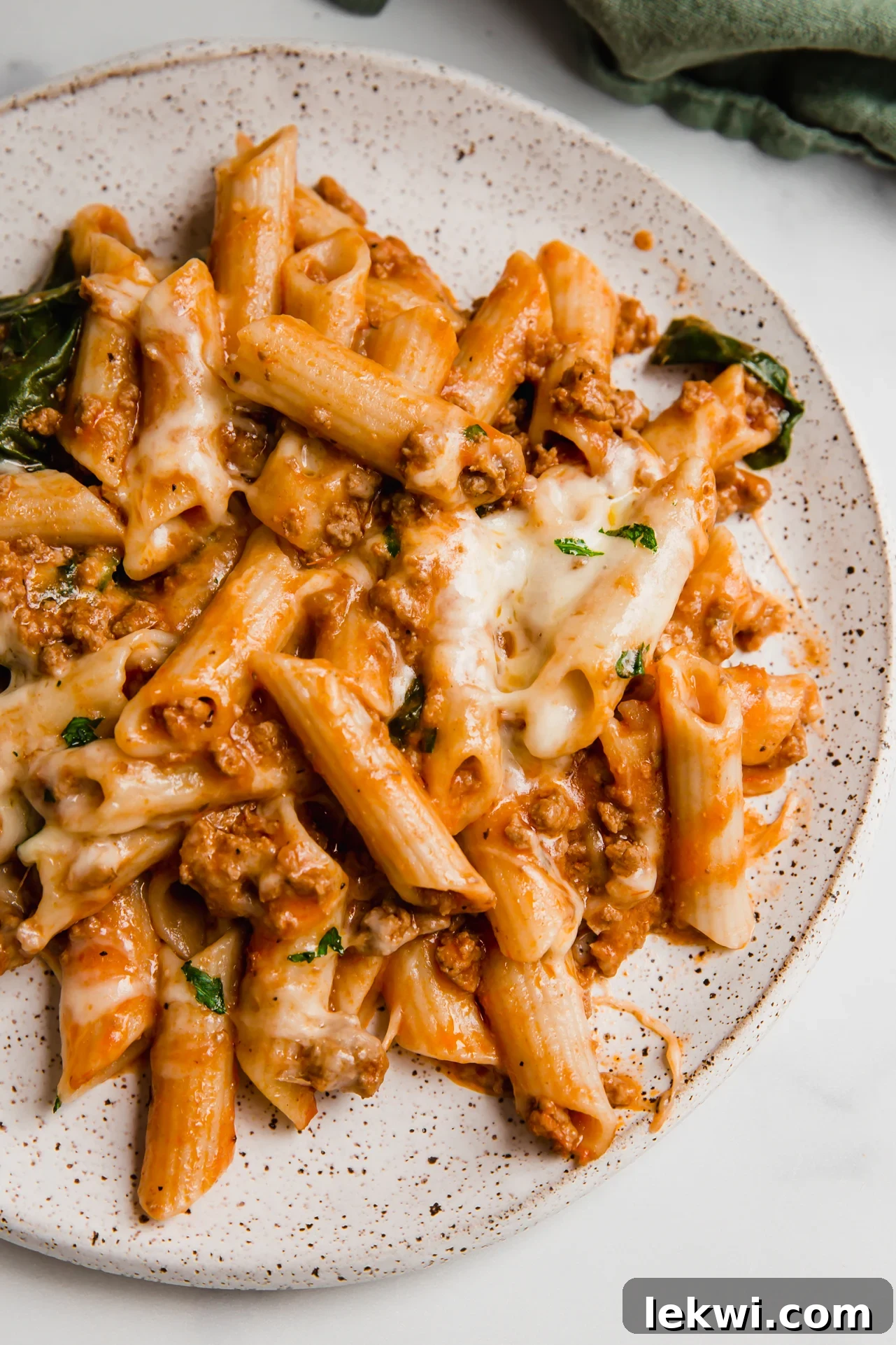 A generous serving of no-boil pasta bake with melted cheese and fresh parsley on a white plate.