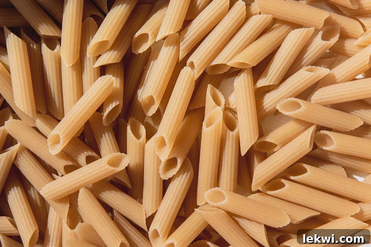 Uncooked gluten-free pasta evenly spread in a greased baking dish, ready for other ingredients.