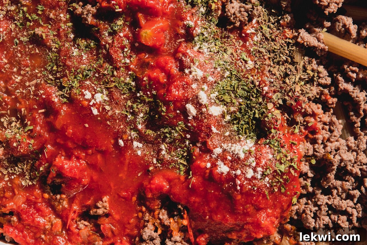 Tomato sauce, chicken broth, and seasonings are poured over the pasta and ground beef in the dish.