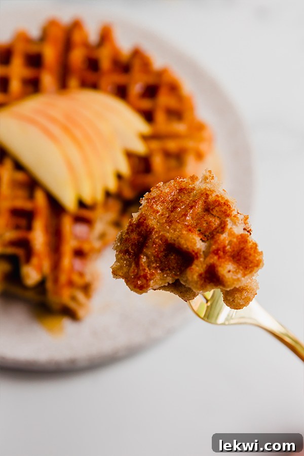 A single bite of gluten-free apple waffle on a fork, showing its fluffy texture.