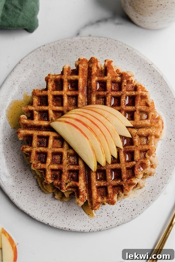 A stack of gluten-free apple waffles with sliced apples and syrup on a plate, ready to be enjoyed.