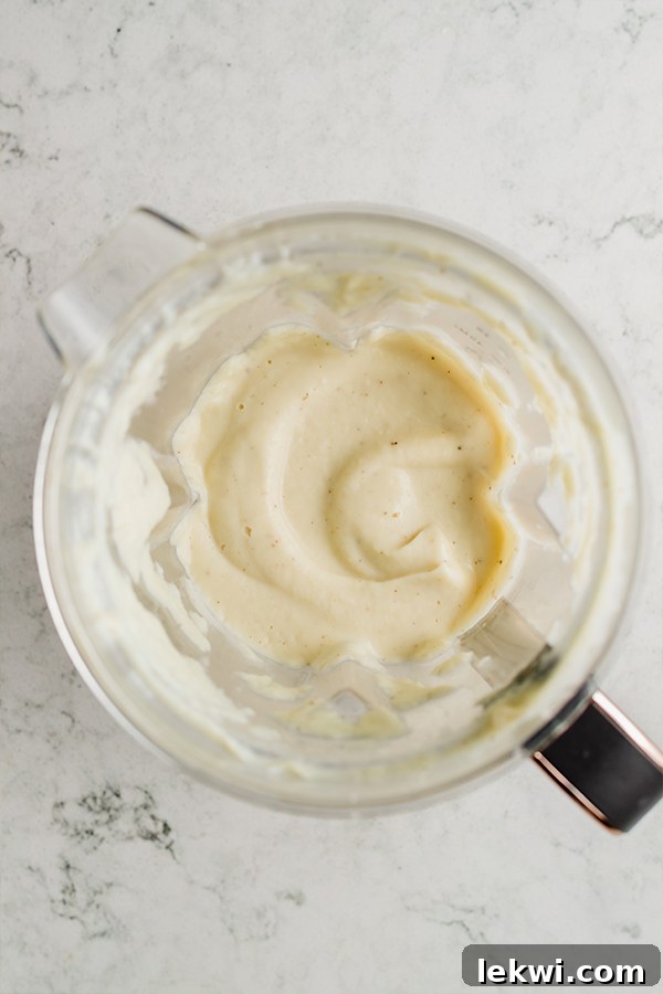 A blender filled with a smooth, creamy cauliflower alfredo sauce, ready to be combined with pasta.